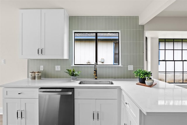 kitchen featuring stainless steel dishwasher, white cabinets, a sink, and light countertops