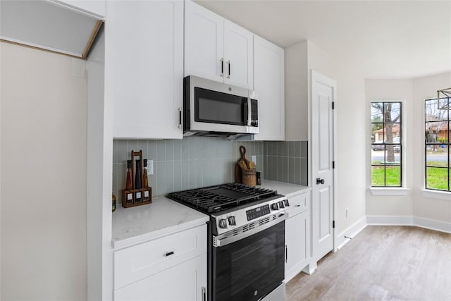927 Peggotty Pl, Austin, TX 78753 - kitchen featuring appliances with stainless steel finishes, tasteful backsplash, white cabinetry, light wood-type flooring, and baseboards