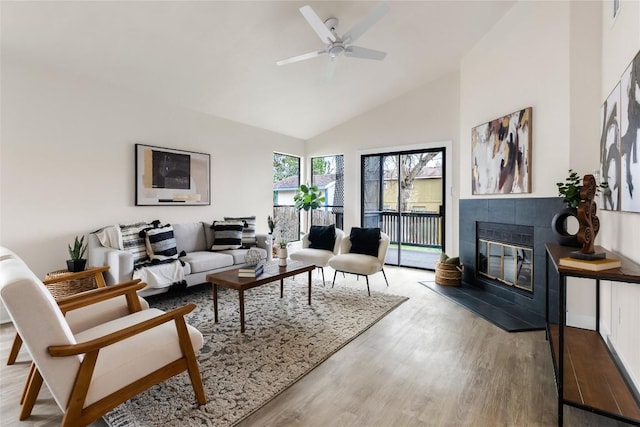 living room with ceiling fan, wood finished floors, high vaulted ceiling, and a tile fireplace