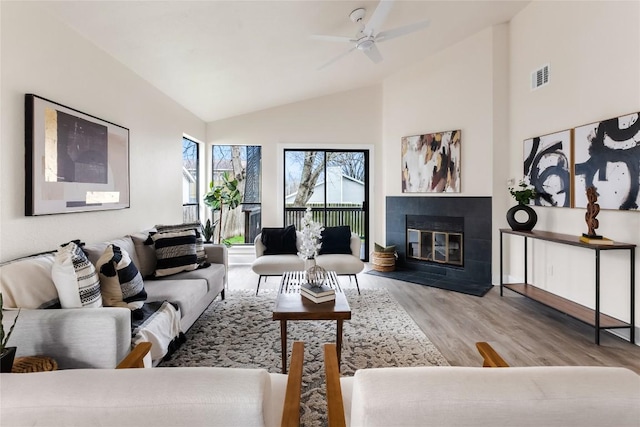 living room featuring ceiling fan, high vaulted ceiling, a tiled fireplace, wood finished floors, and visible vents