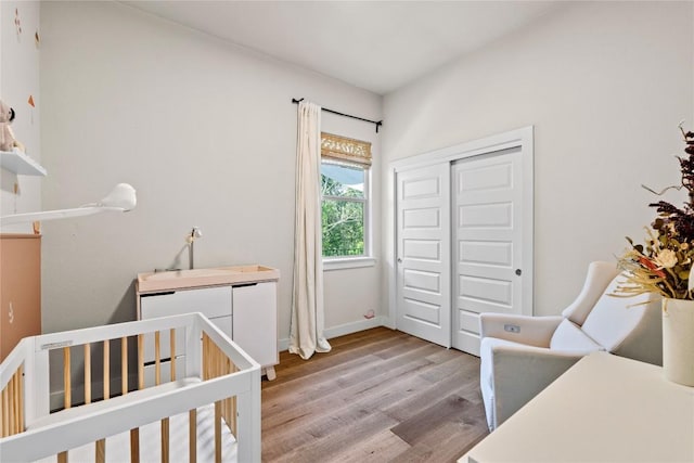 bedroom featuring baseboards, a crib, wood finished floors, and a closet