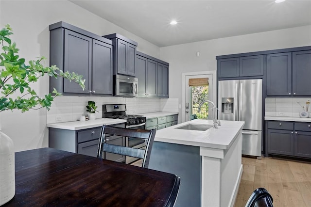 kitchen featuring a sink, light wood finished floors, light countertops, stainless steel appliances, and tasteful backsplash