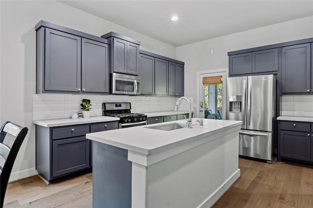 kitchen with a sink, light countertops, light wood-style flooring, stainless steel appliances, and backsplash
