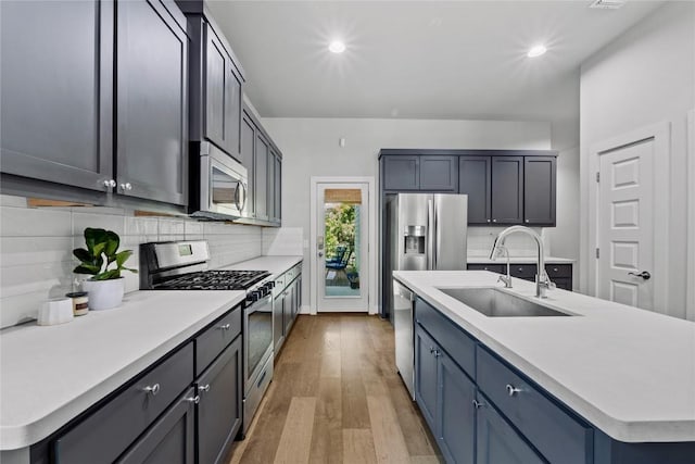 kitchen featuring appliances with stainless steel finishes, decorative backsplash, a sink, and light wood-type flooring