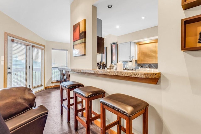 kitchen featuring light countertops, a kitchen breakfast bar, recessed lighting, baseboards, and tasteful backsplash