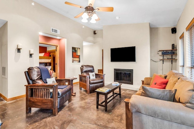 living area featuring ceiling fan, a glass covered fireplace, concrete floors, and baseboards