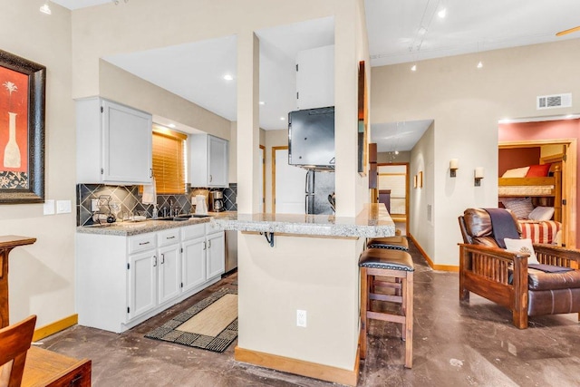 1406 Windsor Rd Unit 305, Austin, TX 78703 - kitchen with finished concrete floors, a breakfast bar, tasteful backsplash, a peninsula, and white cabinetry