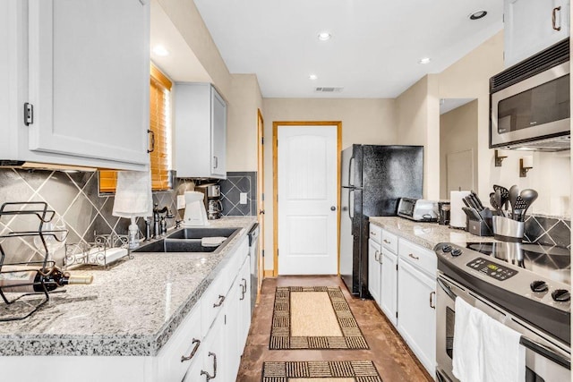 kitchen featuring appliances with stainless steel finishes, a sink, white cabinetry, backsplash, and visible vents