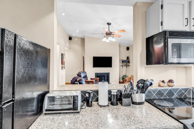 kitchen with light stone countertops, a fireplace, freestanding refrigerator, a ceiling fan, and open floor plan