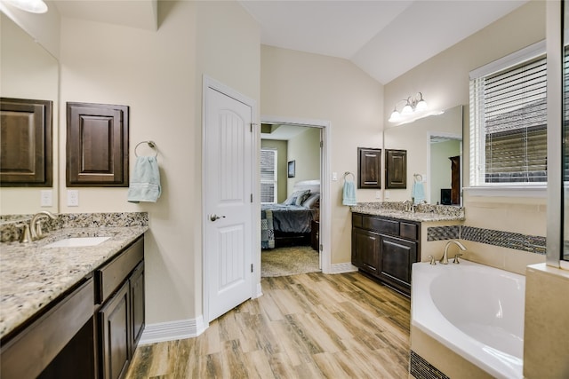 ensuite bathroom with a bath, vaulted ceiling, two vanities, a sink, and connected bathroom