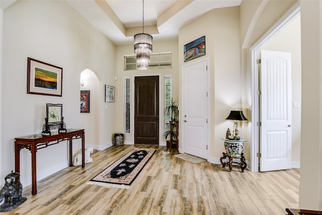 entryway with arched walkways, wood finished floors, baseboards, a raised ceiling, and a high ceiling