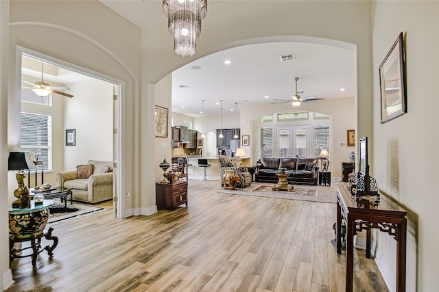 living room with visible vents, arched walkways, light wood finished floors, and a ceiling fan