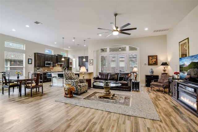 living area featuring arched walkways, a ceiling fan, visible vents, and light wood-style flooring