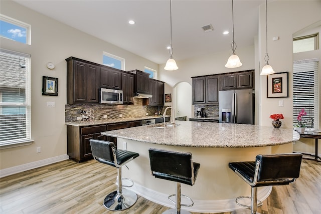 kitchen with decorative backsplash, a sink, baseboards, light wood-style floors, and stainless steel appliances