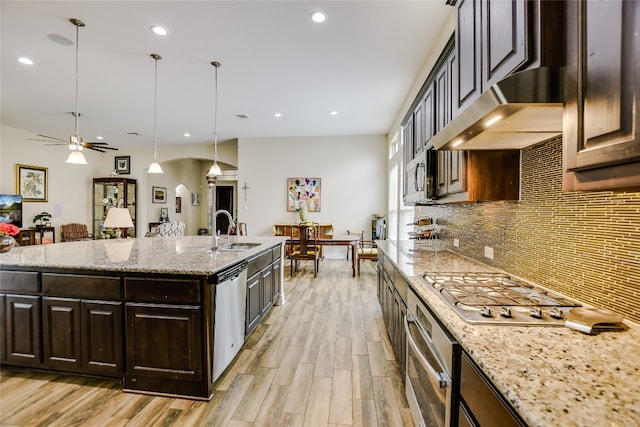 kitchen with a sink, arched walkways, light wood-style flooring, stainless steel appliances, and tasteful backsplash