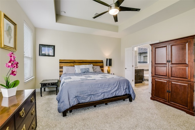 bedroom with connected bathroom, a ceiling fan, a tray ceiling, and light colored carpet