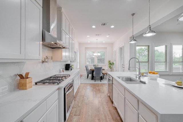 3908 Logan Ridge Dr, Cedar Park, TX 78613 - kitchen featuring a sink, wall chimney range hood, light wood-style flooring, stainless steel appliances, and white cabinets