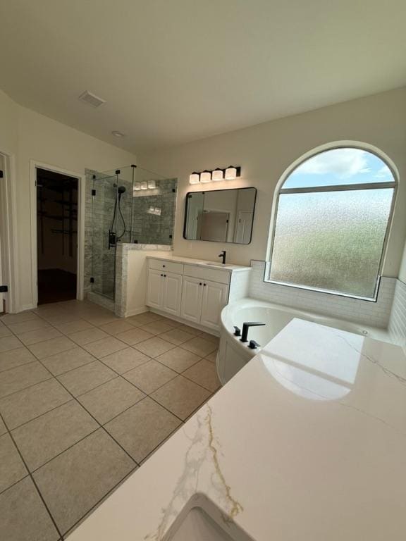 full bath with a walk in closet, a bathtub, tile patterned flooring, a stall shower, and vanity