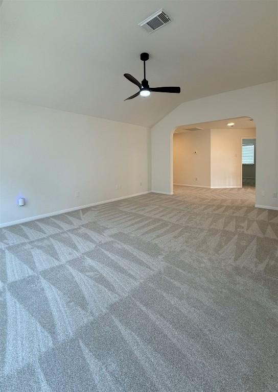empty room featuring arched walkways, vaulted ceiling, light carpet, and visible vents