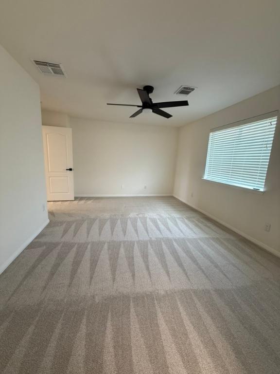 carpeted empty room featuring a ceiling fan, baseboards, and visible vents