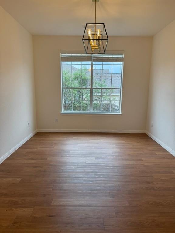 empty room featuring baseboards, a notable chandelier, and wood finished floors