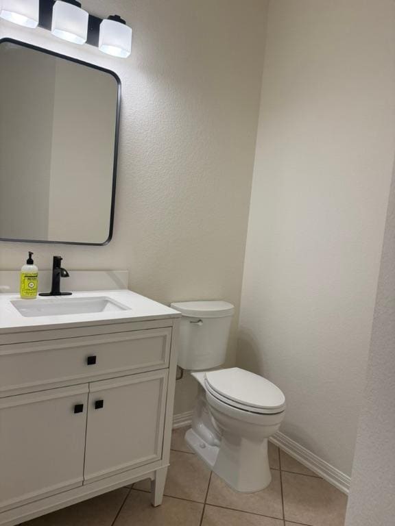 half bathroom with baseboards, tile patterned flooring, vanity, and toilet