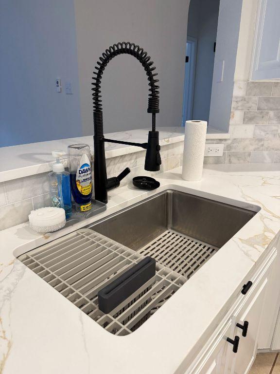 interior details with a sink, light stone countertops, and white cabinetry