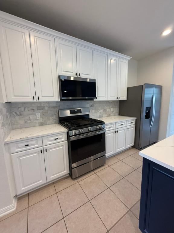 kitchen featuring decorative backsplash, light stone countertops, white cabinets, light tile patterned floors, and stainless steel appliances