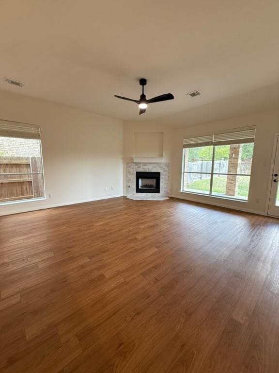 unfurnished living room with ceiling fan, a fireplace, wood finished floors, and visible vents