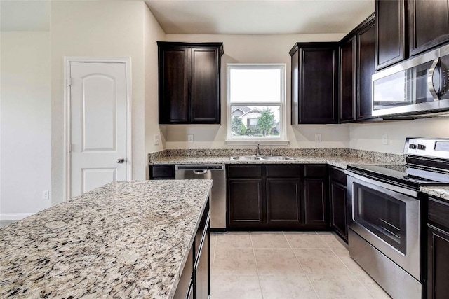 1139 Amy Dr, Kyle, TX 78640 - kitchen with dark brown cabinetry, appliances with stainless steel finishes, light stone counters, a sink, and light tile patterned floors