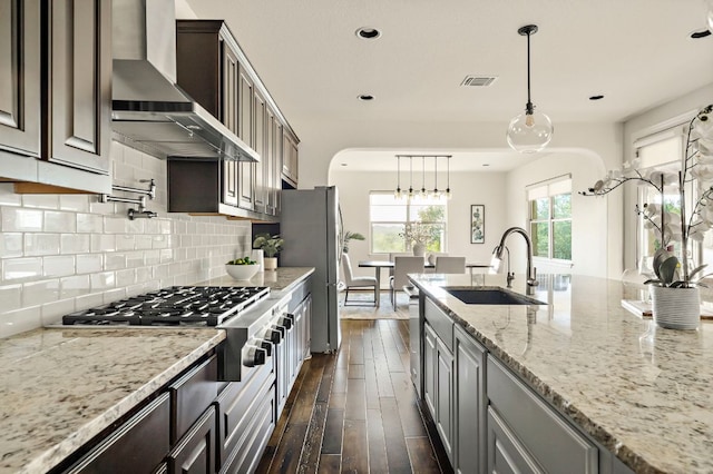 kitchen featuring visible vents, dark wood-style flooring, wall chimney exhaust hood, a sink, and appliances with stainless steel finishes