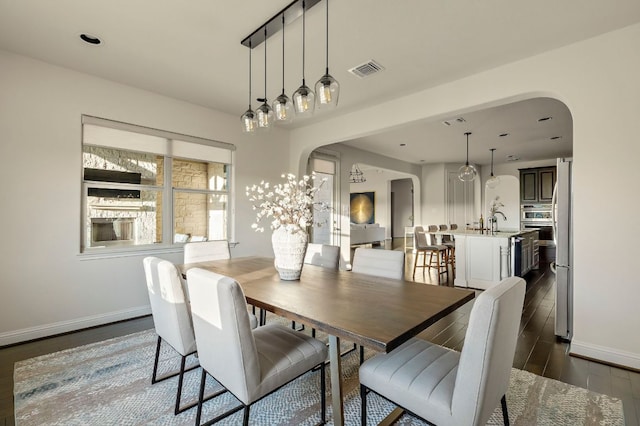 dining area with visible vents, arched walkways, dark wood-style flooring, and baseboards