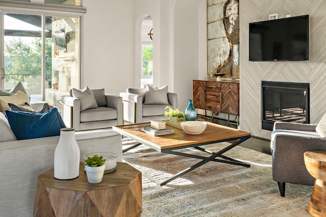 living room with arched walkways, a glass covered fireplace, and wood finished floors