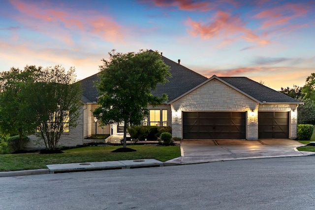 view of front of house featuring roof with shingles, a lawn, a garage, concrete driveway, and stone siding