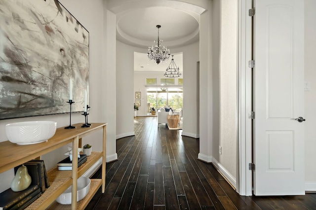 corridor featuring an inviting chandelier, baseboards, dark wood-style floors, and a raised ceiling