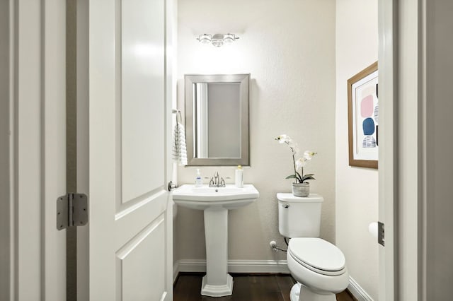 half bathroom with toilet, baseboards, and wood finished floors