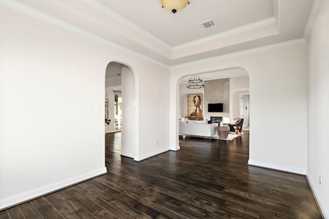 empty room featuring visible vents, ornamental molding, wood finished floors, a fireplace, and a tray ceiling