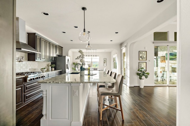 kitchen with dark wood-style floors, wall chimney exhaust hood, tasteful backsplash, a sink, and stainless steel appliances
