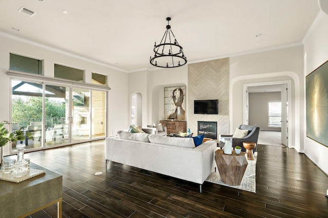 living area with dark wood-style flooring, an inviting chandelier, arched walkways, a tile fireplace, and ornamental molding