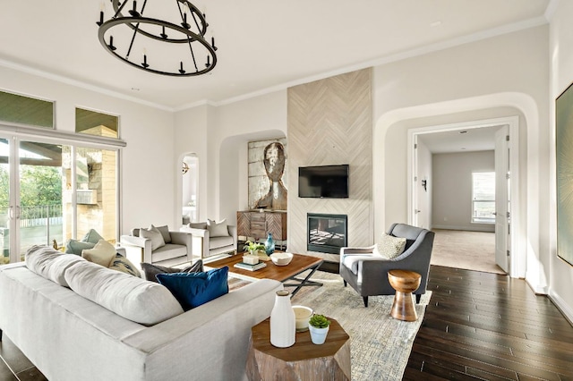 living room featuring crown molding, a notable chandelier, a fireplace, arched walkways, and dark wood-style floors