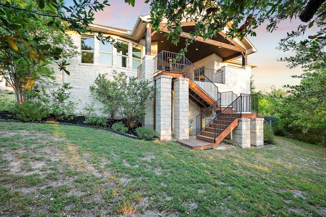 property exterior at dusk with stairs, a yard, and stone siding
