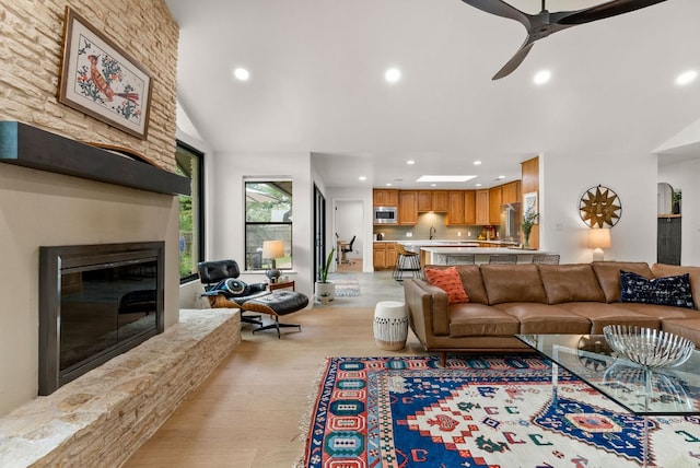 living room featuring light wood-style floors, a ceiling fan, recessed lighting, and a stone fireplace