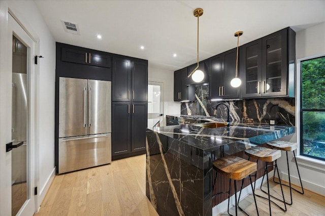 1121 Reagan Ter, Austin, TX 78704 - kitchen featuring high end fridge, dark cabinetry, a peninsula, a breakfast bar, and light wood-type flooring