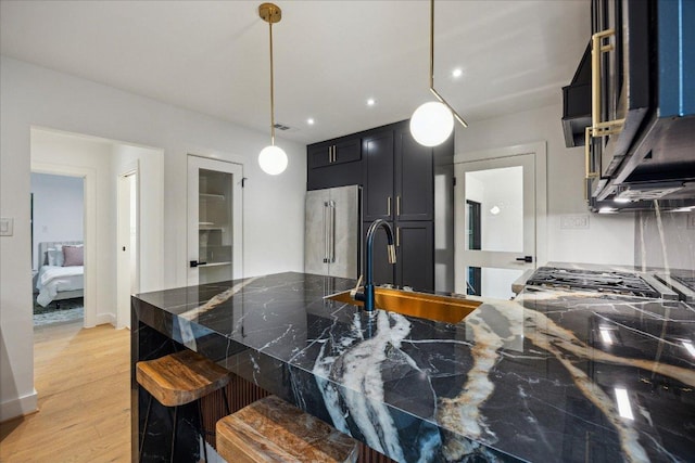 kitchen with a breakfast bar area, hanging light fixtures, light wood-type flooring, dark cabinets, and high end fridge