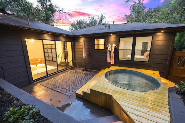 back of property at dusk with a hot tub and roof with shingles
