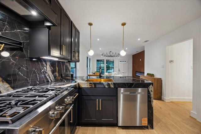 1121 Reagan Ter, Austin, TX 78704 - kitchen featuring appliances with stainless steel finishes, a peninsula, tasteful backsplash, light wood finished floors, and decorative light fixtures