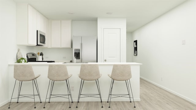 kitchen with stainless steel microwave, refrigerator with ice dispenser, a breakfast bar, and light wood-style flooring