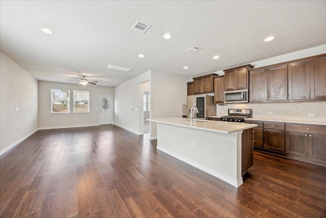 kitchen with visible vents, a center island with sink, dark wood finished floors, backsplash, and stainless steel appliances
