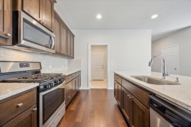 kitchen featuring decorative backsplash, light stone countertops, dark wood-type flooring, a sink, and appliances with stainless steel finishes