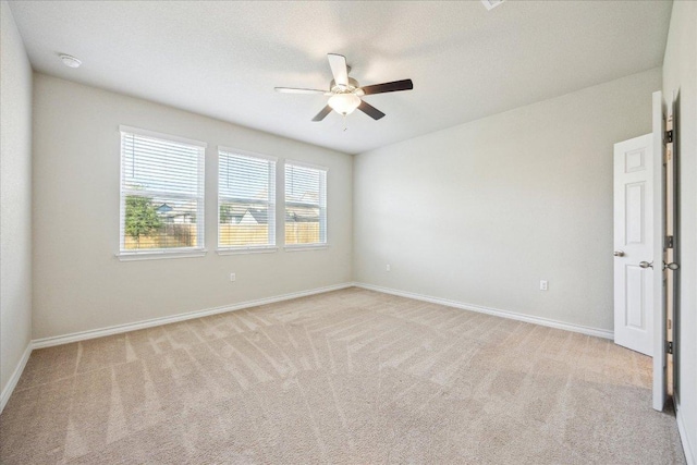spare room with a ceiling fan, baseboards, and light colored carpet